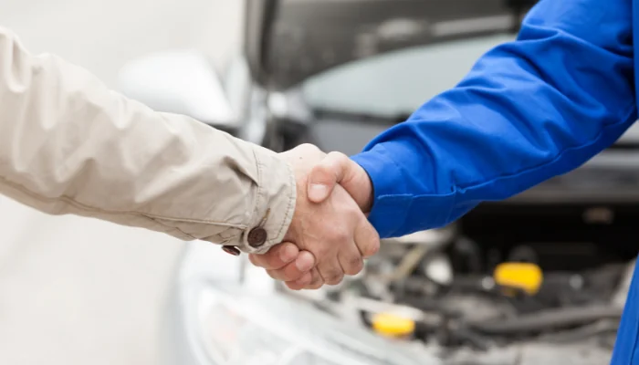 Aperto de mãos entre duas pessoas com um carro atrás representando cobertura completa.