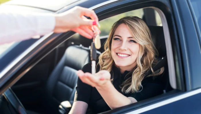 Quais São as Coberturas Oferecidas pelo Seguro Auto por Assinatura para carros novos e usados representado por uma mulher em um carro recebendo uma chave em mãos.