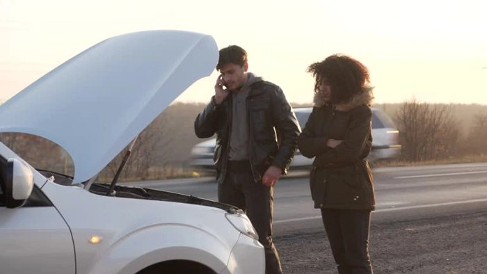 Homem e mulher observam dentro do capô de um carro, enquanto o homem fala ao celular. Falando sobre o melhor seguro de carro para não ficar na mão.