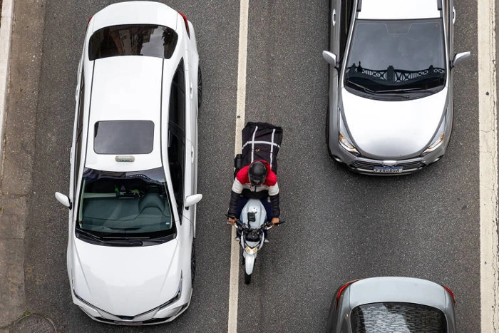 Moto passando em meio a duas fileiras de carro no trânsito urbano. Falando sobre seguro obrigatório para carro.