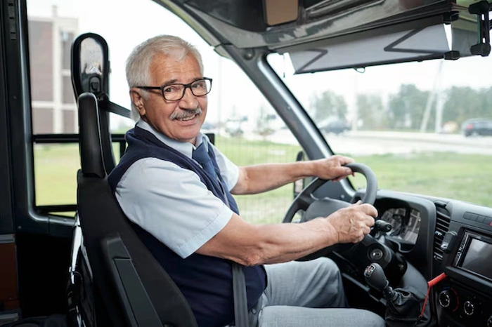 Idoso sorridente com as mãos no volante de um ônibus. Explicando se seguro de carro para idoso é mais barato.