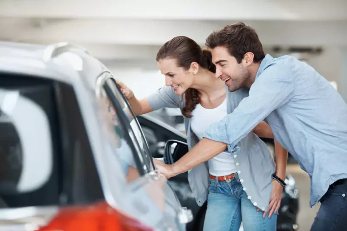 Casal sorridente olha para o interior de um carro através do seu vidro lateral. Explicando como fazer um consórcio de carros.