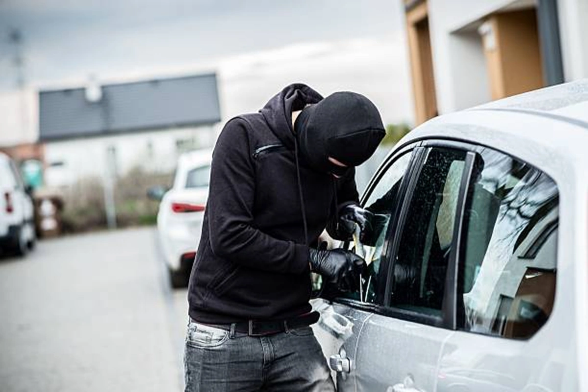 Criminoso tentando arrombar carro estacionado na rua. Falando sobre os carros menos roubados no brasil.