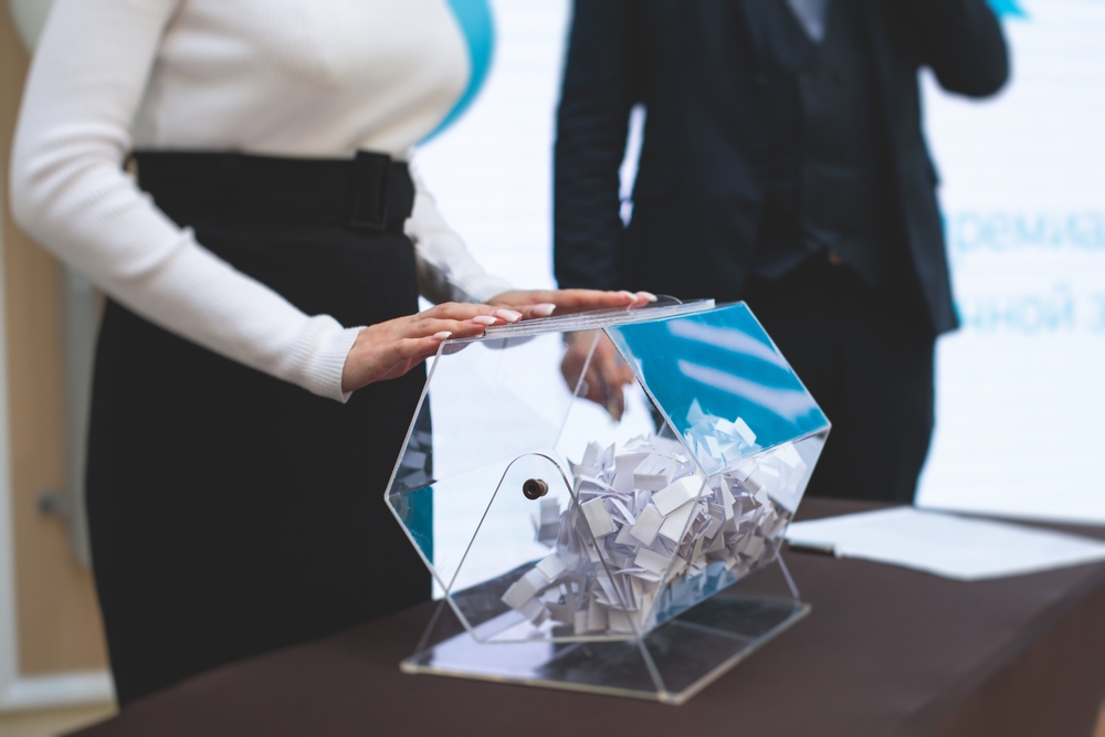 Mulher manipula equipamento de fazer sorteios. Falando sobre quanto tempo leva para ser contemplado no consórcio de carro.
