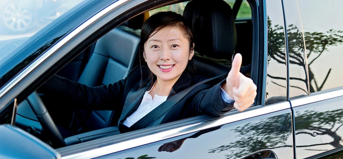 Condutora faz sinal de positivo de dentro de seu veículo. Falando sobre o seguro auto flexível.