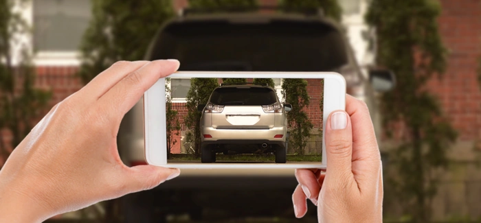 Pessoa tira fotos da traseira de um veículo com seu smartphone. Falando sobre como fazer seguro auto online.