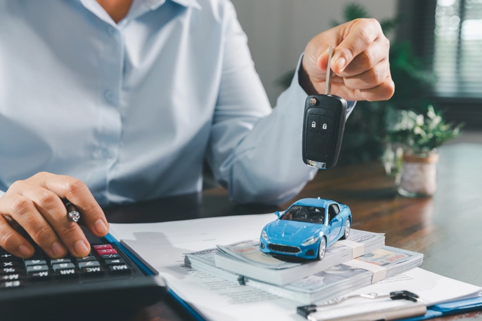 Homem manipula calculadora, miniatura de carro na cor azul, chave de carro e documentos. Falando sobre azul seguro auto leve.