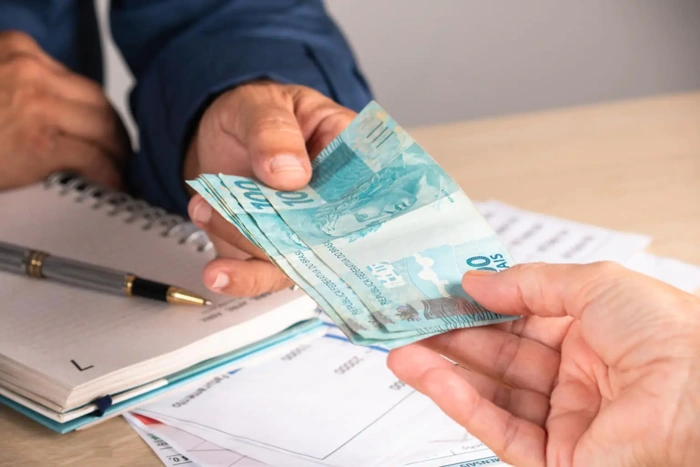 Pessoa entregando maço de dinheiro a outra. Falando sobre ressarcimento por valor pago em consórcio.