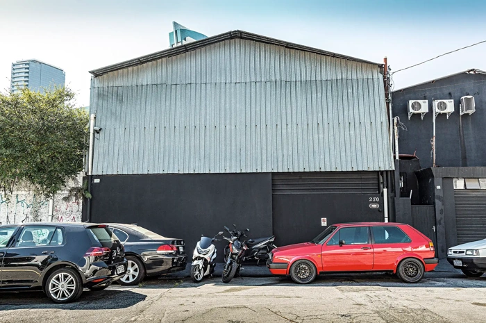 Carros e motos estacionados em frente a um galpão garagem. Falando sobre seguro de carros sem garagem.